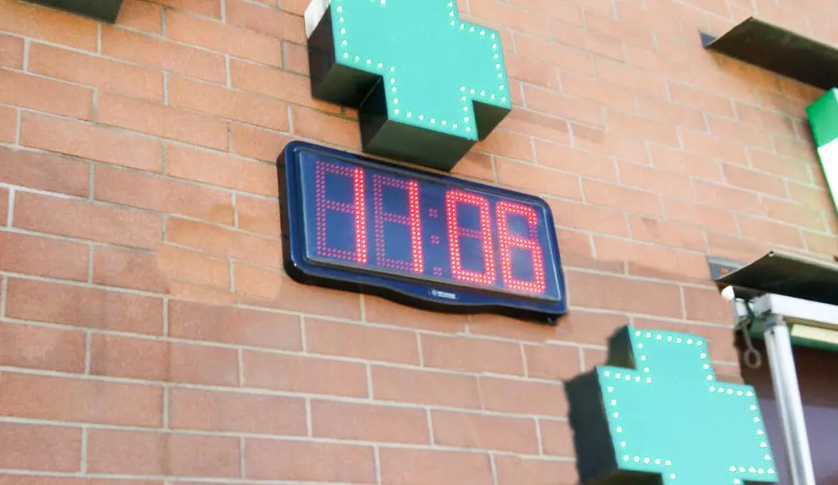Orologio a LED rosso a parete accanto alle croci verdi di una farmacia