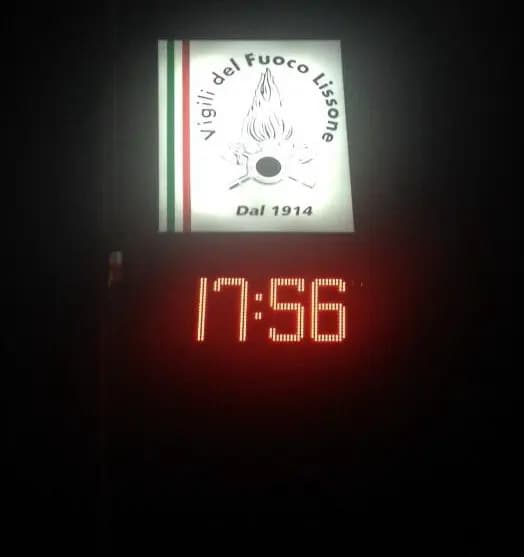 Orologio a LED acceso di notte sotto l’insegna luminosa di una caserma dei vigili del fuoco